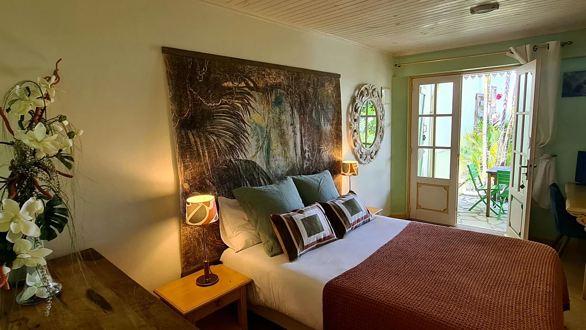 Une chambre de la case, son lit, son grand tableau et la porte sur le jardin