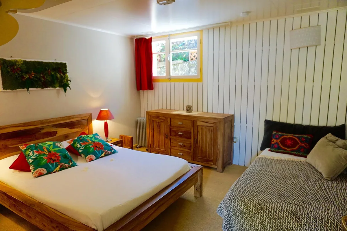 Une chambre aux coussins rouges et sa fenêtre sur le jardin