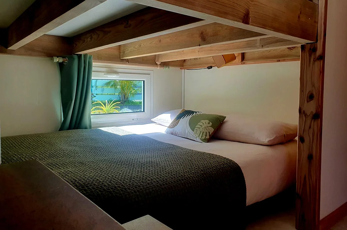 Un lit du lodge sous les poutres et son rideau vert