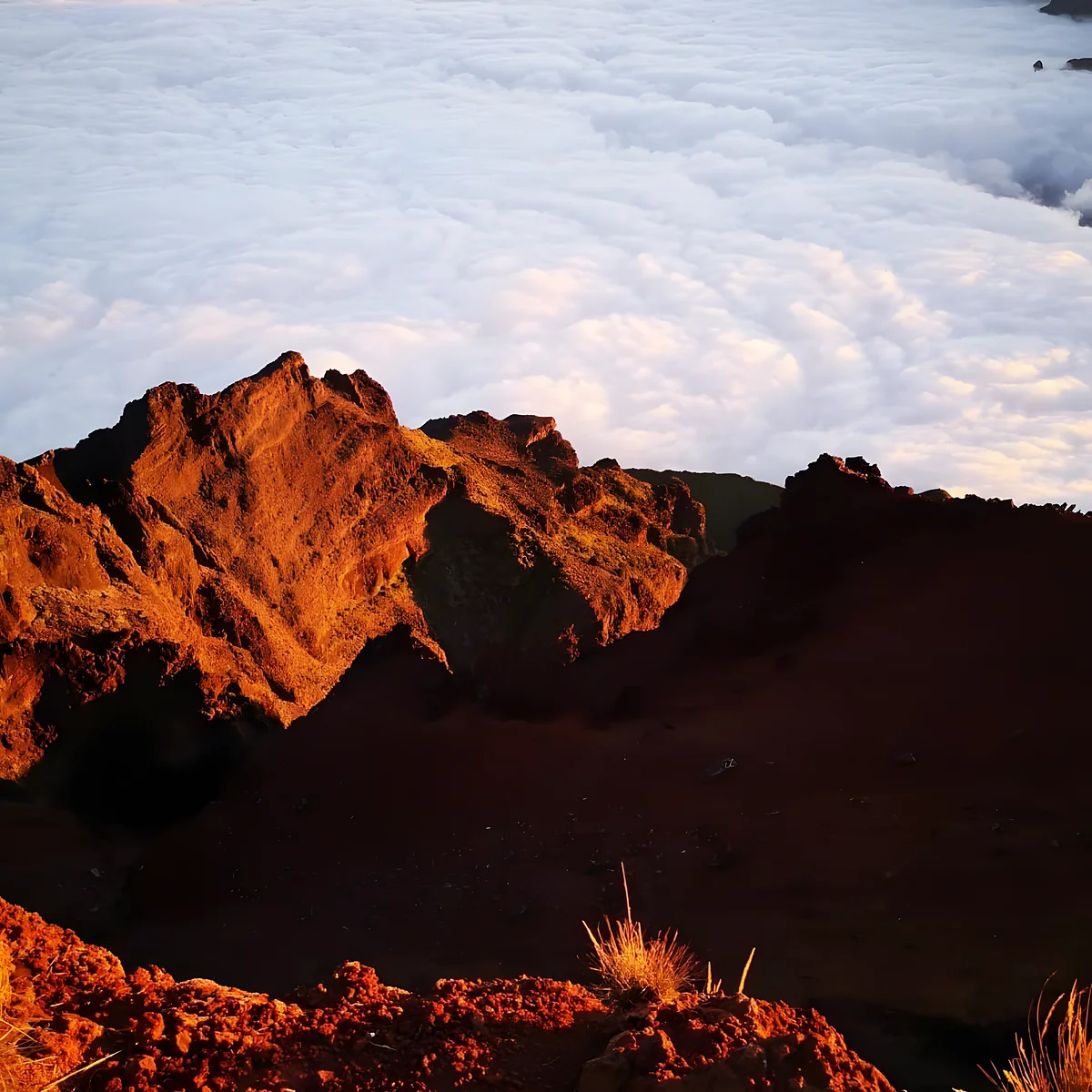 Un sommet du cirque rougi par le soleil couchant, au-dessus de la mer de nuages