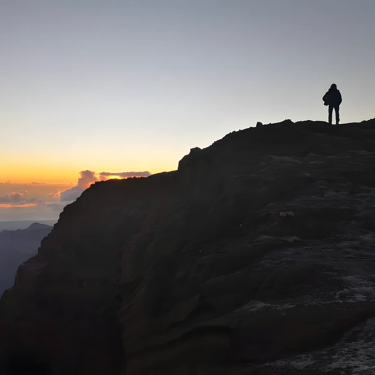 Un randonneur au sommet, face au lever du soleil au-dessus des nuages